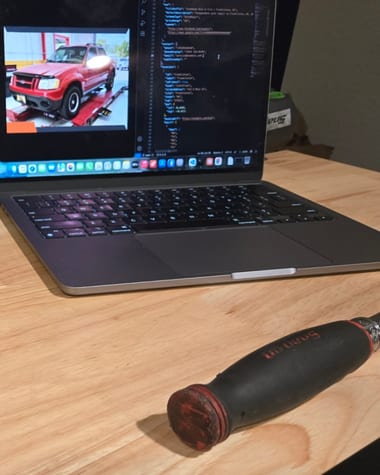 A worn Snap-on screwdriver on a workbench beside a laptop showing the code behind an auto repair shop's website.